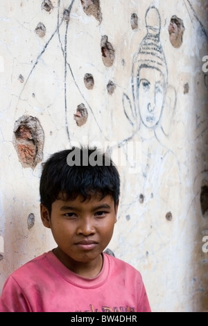 A 9 anno di età del ragazzo è in piedi da una parete con pock contrassegni effettuati dai Khmer rossi proiettili al Wat Bangkok in Kampong Cham, Cambogia.