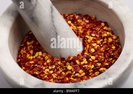 Grigio e bianco il pestello e mortaio riempito con il giallo e il rosso piccante peperoncino essiccato in scaglie Foto Stock