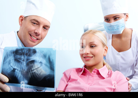 Ritratto di donna con un dentista che mostra la sua fotografia a raggi x, dietro assistant Foto Stock