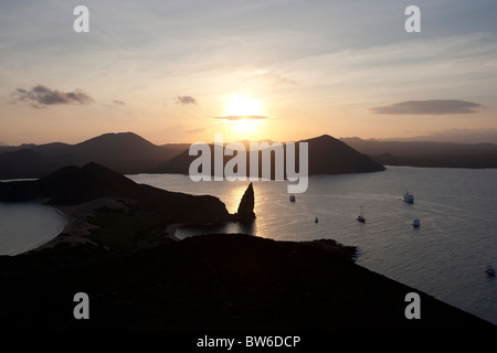 Vista del pinnacolo di roccia e tour ormeggiate imbarcazioni al tramonto dalla cima di un vulcano, Bartolome Island, Galapagos. Foto Stock