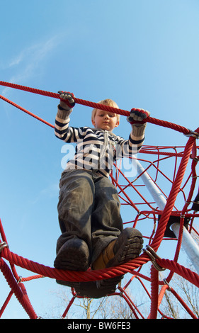Un bambino biondo ragazzo di 4 anni su un parco giochi estivo Arrampicate salire la corda net Foto Stock