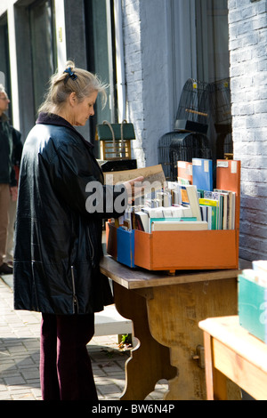 Una donna accede attraverso la seconda mano libri al di fuori di un negozio vintage di Anversa in Belgio Foto Stock