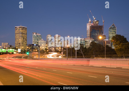 Sentieri di luce sulla superstrada Mitchell con dello skyline di Perth, Western Australia, in background Foto Stock