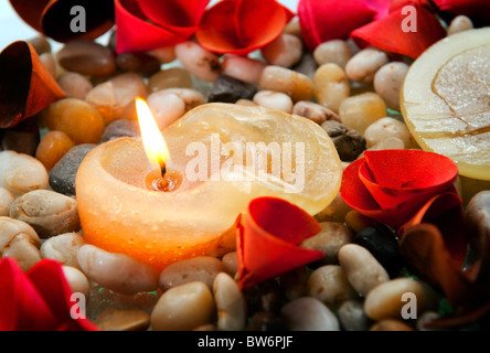 Una candela che brucia tra le pietre piccole e luminose petali Foto Stock