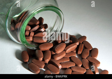 Le pillole generiche fuoriuscita di una bottiglia di vetro chiaro Foto Stock