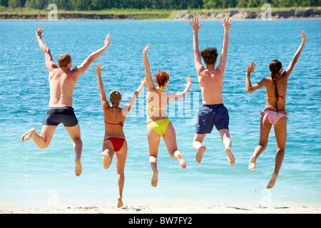 Un gruppo di persone con le mani in alto saltando nel lago Foto Stock
