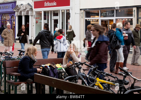 Due giovani donne mangiare take away pasties su un high street panchina Foto Stock
