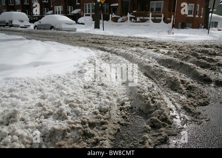 dirty snow on a plowed city side street with tire tracks in winter Foto Stock