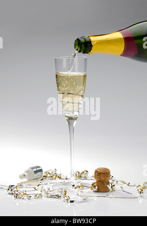 Un singolo bicchiere di champagne versata da una bottiglia su uno sfondo bianco con popper e streamers Foto Stock