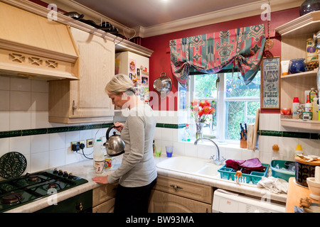 La donna in cucina versando un bollitore Foto Stock