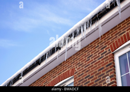 Immagine invernale di ghiaccioli appesi da grondaia sulla coperta di neve tetto di una casa moderna. Foto Stock