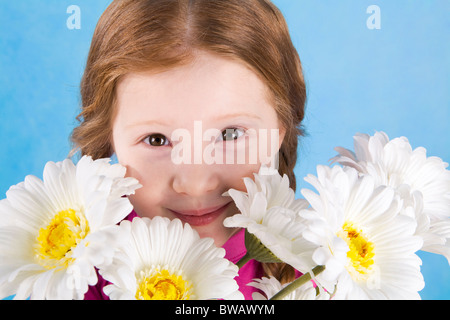 Ritratto di ragazza carina guardando da dietro la molla fiori su sfondo blu Foto Stock