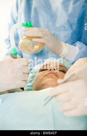 Foto del giovane paziente femmina con gli occhi chiusi prima di funzionamento con le mani di chirurghi su di lei Foto Stock