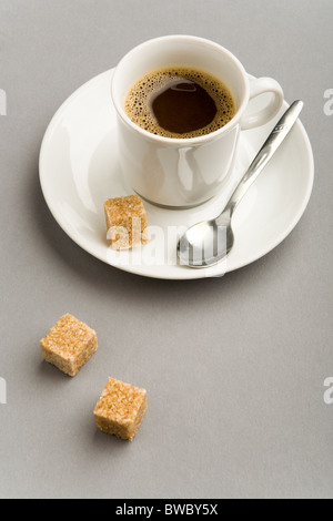 Immagine della tazza bianca piena di forte caffè nero e due pezzi di zucchero di canna nei pressi di Foto Stock