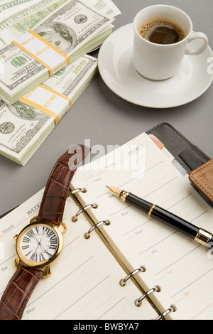 Immagine di aprire il blocco note con penna stilografica e guardare su di esso con la tazza di caffè e banconote di dollari nelle vicinanze Foto Stock