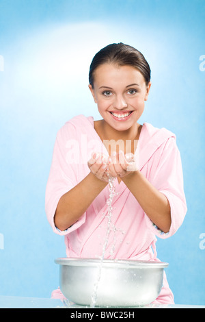 Ritratto di felice femmina in accappatoio rosa gli spruzzi di acqua dal lavandino Foto Stock