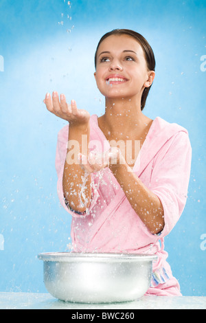 Ritratto di donna felice in rosa accappatoio spruzzi d'acqua su sfondo blu Foto Stock