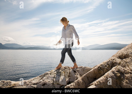 Donna che cammina sulla spiaggia rocciosa e dal mare Foto Stock