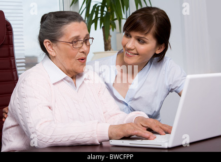 Ritratto di giovane ragazza guardando la nonna con sorriso mentre quest'ultima digitazione sulla tastiera del notebook Foto Stock