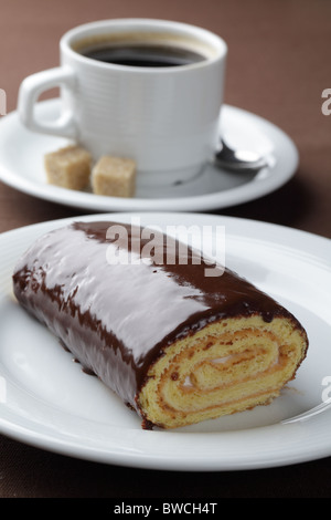 Rotolo svizzero con ripieno di panna e cioccolato topping contro una tazza di caffè nero Foto Stock