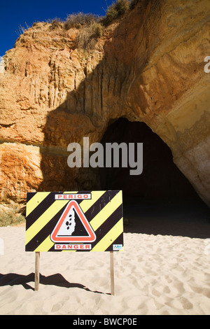 Un segno di avvertimento di caduta di sassi nella parte anteriore di una grotta sulla spiaggia di Praia da Rocha. Foto Stock