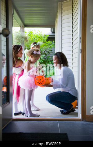 Stati Uniti d'America, Illinois, Metamora, giovane donna dando caramelle per ragazze (6-7, 8-9) in costumi durante il periodo di Halloween Foto Stock