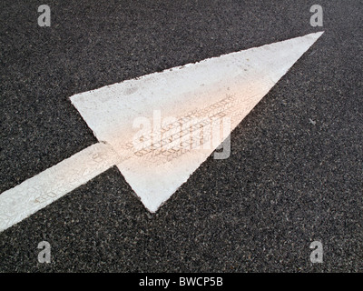 Freccia bianca sulla strada che indica la direzione per il traffico a seguire. Marchio di pneumatici integrati in vernice sulla freccia. Foto Stock