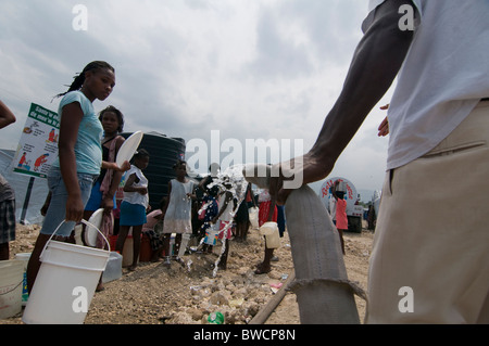 La gente in coda per alimentazione di acqua tramite la Croce Rossa in corrispondenza di una casa temporanea composto impostato per i superstiti del terremoto a Port au Prince dopo un terremoto di magnitudine 7.0 ha colpito Haiti il 12 gennaio 2010 Foto Stock