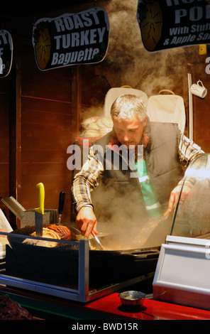 L'uomo cucina tradizionale la carne di maiale e la Turchia ad un mercatino di natale in stallo in Portsmouth Inghilterra Regno Unito Foto Stock