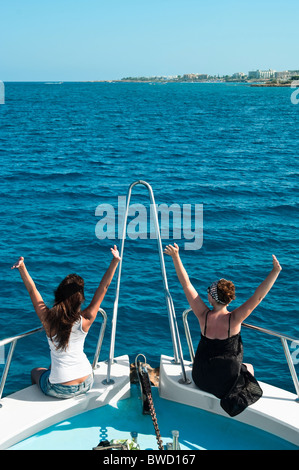 Due giovani donne sulla poppa della barca in mare blu Holding Hands Up Foto Stock