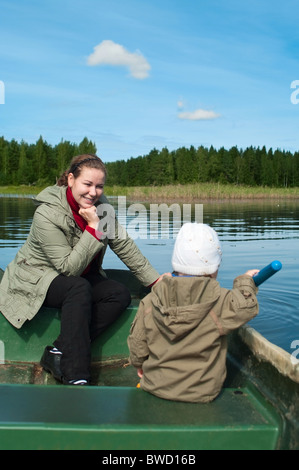 Madre e figlio insieme ride in una barca a remi su un lago nel bosco. Irriconoscibile il bambino non è a fuoco Foto Stock