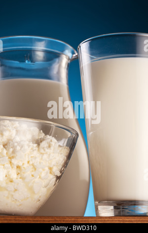 Vaso in vetro e con il latte e la ciotola con il formaggio. Isolato su un blu. Foto Stock