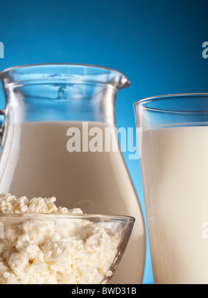 Il vaso e un bicchiere di latte e ciotola con il formaggio. Isolato su un blu. Foto Stock