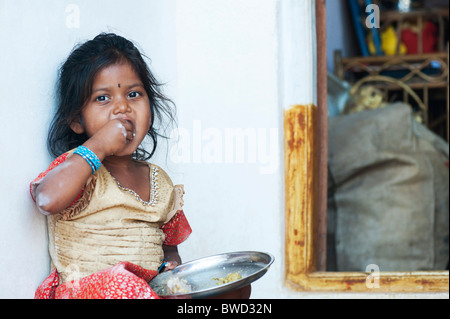 Indiano piccolo villaggio rurale ragazza mangia stracci palla per colazione, alla porta di casa sua. Andhra Pradesh, India Foto Stock