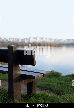 Banco di vuoto che si affaccia su un lago con case a distanza al di fuori della messa a fuoco. Foto Stock