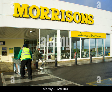 Un Morrisons dipendente del negozio spingendo supermercato trollies Foto Stock