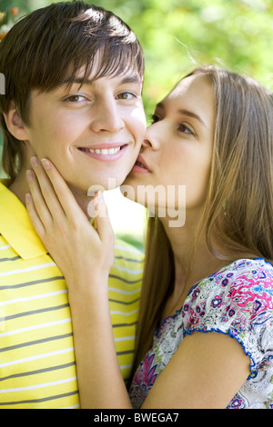 Bella ragazza baciare teneramente il suo fidanzato mentre egli sorride alla fotocamera Foto Stock