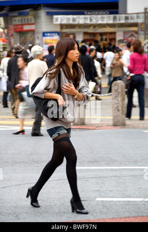 Una giovane donna di attraversare una via in Shibuya, Tokyo, Giappone Foto Stock
