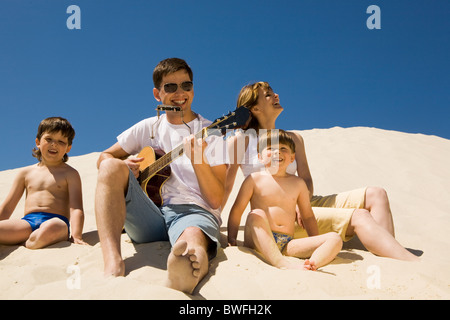 Ritratto di Allegro uomo suonare la chitarra con i suoi figli e la moglie di vicino e godersi la musica Foto Stock