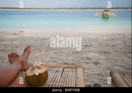 Piedi di turista accanto alla tradizionale noce di cocco, Gili Trawangan isola, isole Gili, Indonesia Foto Stock