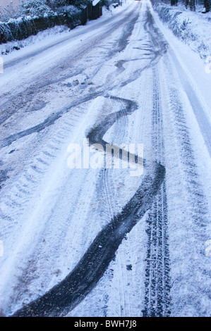 Tracce di pneumatici che mostra come una vettura scivolato e fatto scorrere su un ghiacciate, innevate road Foto Stock