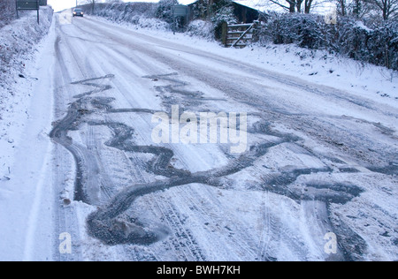 Skid e segni di slittamento realizzato da un auto su un gregge di ghiacciate, innevate road Foto Stock