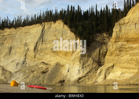 Il Camp, tenda e canoa su una barra di ghiaia, alta cut bank, fiume cliff, erosione, dietro, superiore Liard River, Yukon Territory, Canada Foto Stock