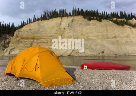 Il Camp, tenda e canoa su una barra di ghiaia, alta cut bank, fiume cliff, erosione, dietro, superiore Liard River, Yukon Territory, Canada Foto Stock