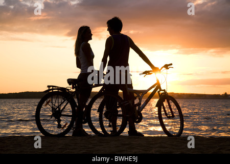 Coppia giovane permanente sulla riva del mare con le loro biciclette e guardando ogni altro Foto Stock