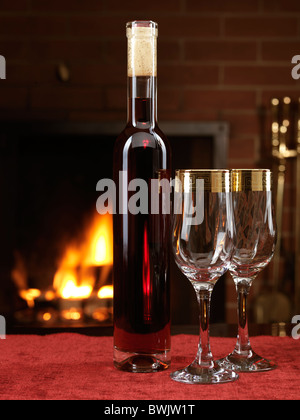Bottiglia di vino rosso secco e due bicchieri di vino su una tabella con un camino in background Foto Stock