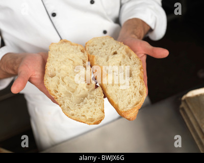 Baker che mostra una bella struttura porosa di un pane appena sfornato tagliate a metà Foto Stock