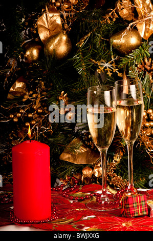 Due bicchieri di champagne, christmas candle, presenta e decorazioni su un albero. Rosso verde e oro. Foto Stock
