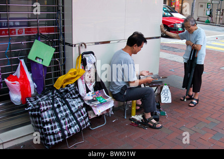 Uomo cinese di Hong Kong in angolo di strada affilatura utensili e coltelli per i clienti mentre sono in attesa Foto Stock