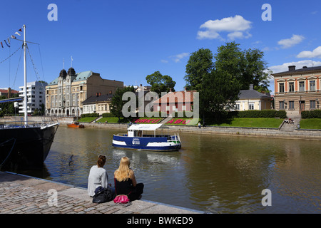 Due giovani donne seduta sulle sponde del fiume Aurajoki, Turku, Finlandia Foto Stock